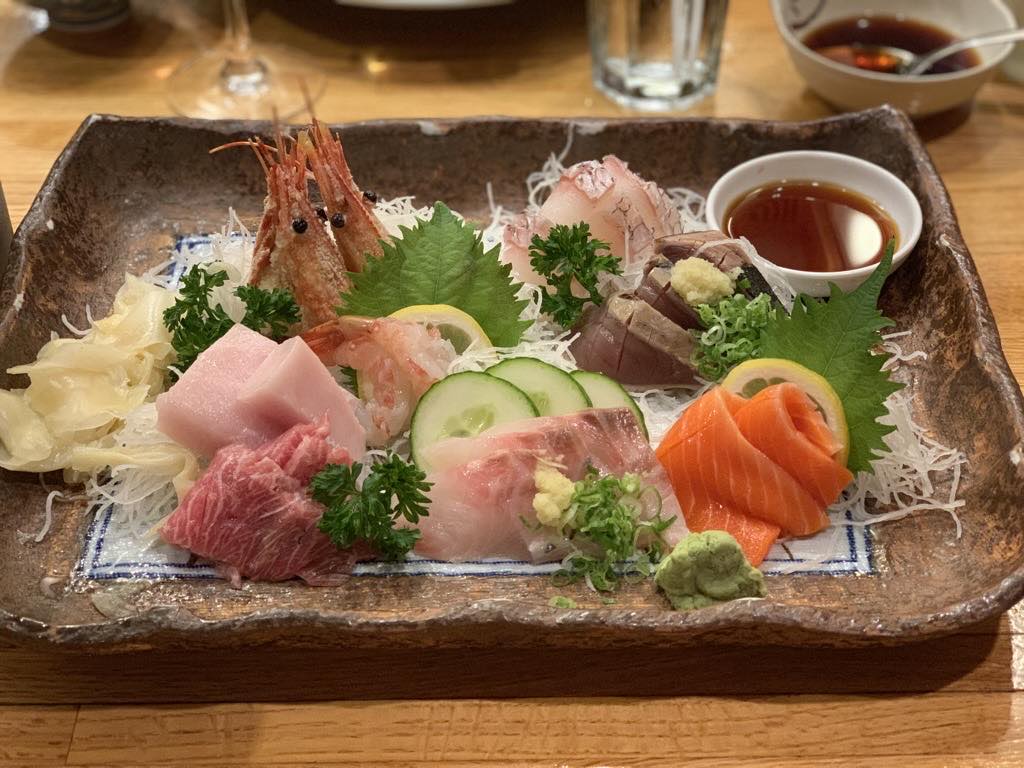 A sashimi platter at Akai Hana with tuna, salmon, shrimp, and wasabi on a stone plate