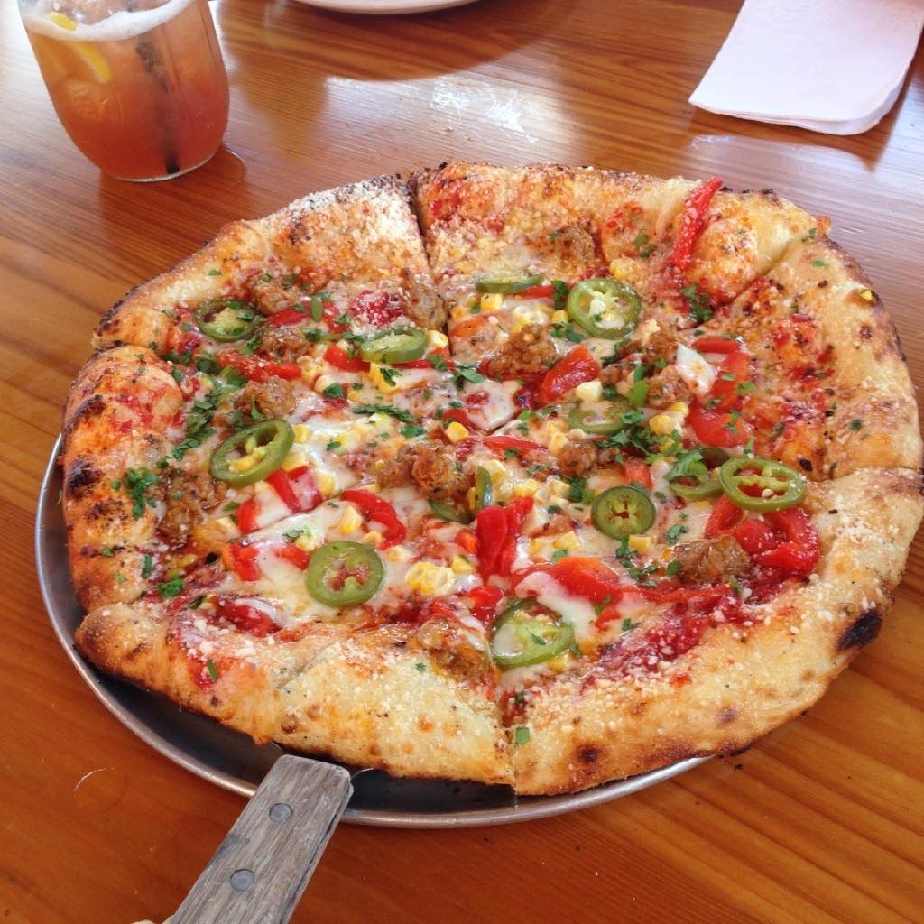 A Harvest Pizzeria pizza topped with sausage, jalapenos, red peppers, and corn