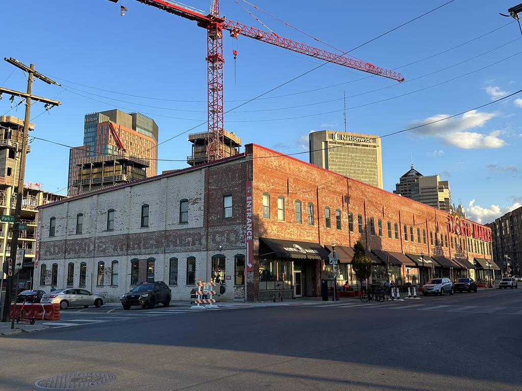 The North Market building at dusk with the downtown Columbus skyline and a construction crane behind it