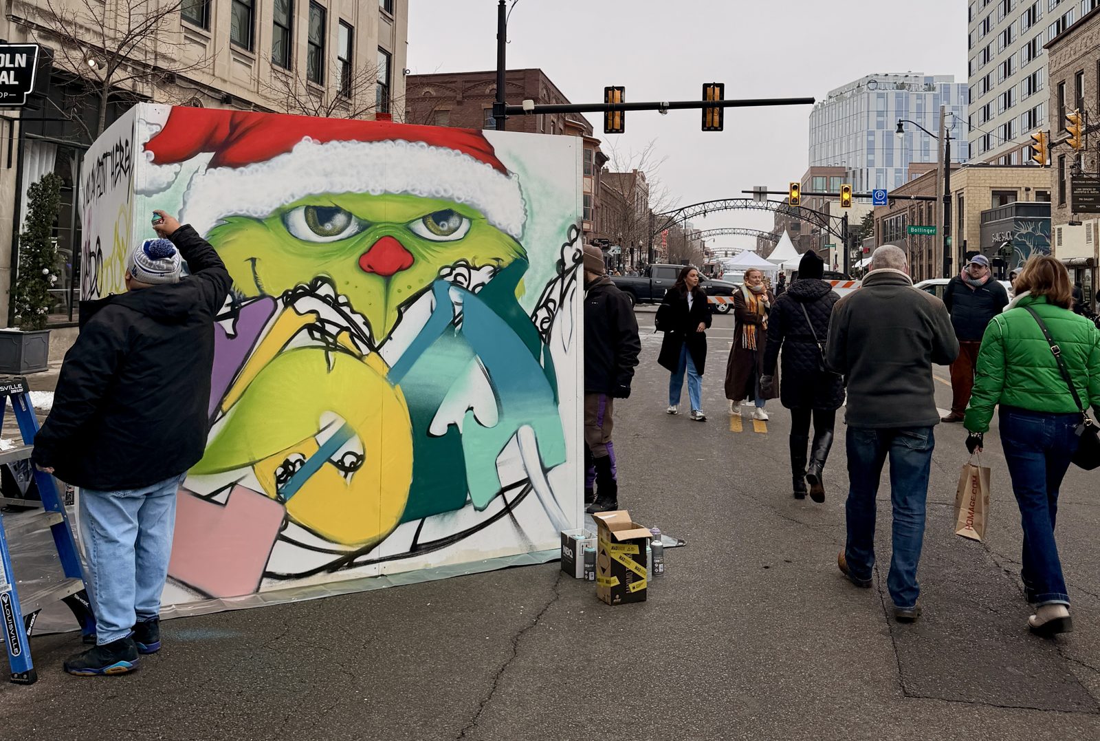An artist painting a large Grinch mural in the middle of a car-free High Street in the Short North